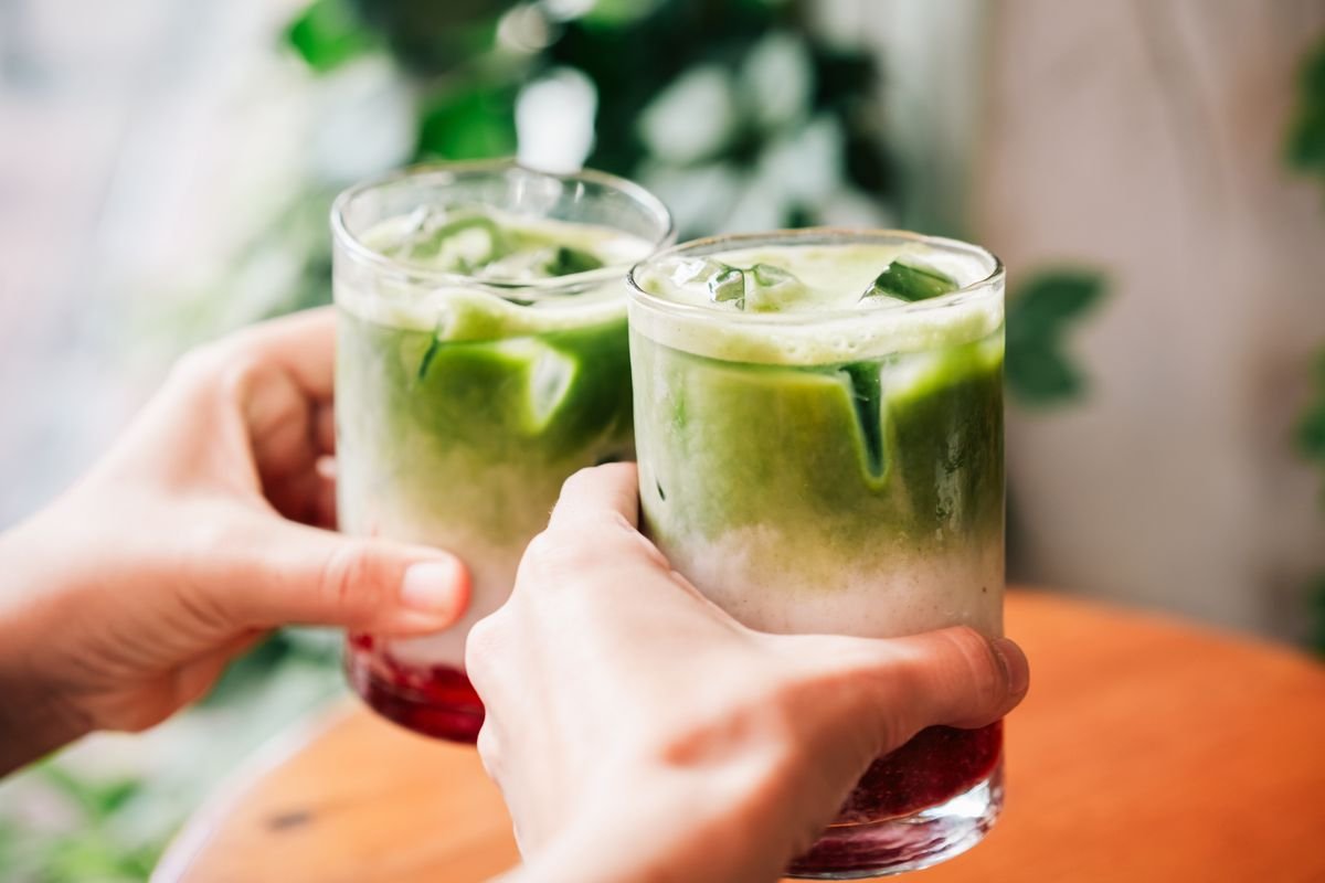 matcha latte ត្រជាក់​ជាមួយ​ស៊ីរ៉ូ​បឺរី​ក្រហម​បម្រើ​ក្នុង​កែវ​ថ្លា​ដាក់​លើ​តុ​ឈើ​ក្នុង​បរិយាកាស​ហាង​កាហ្វេ​ដ៏​កក់ក្ដៅ។