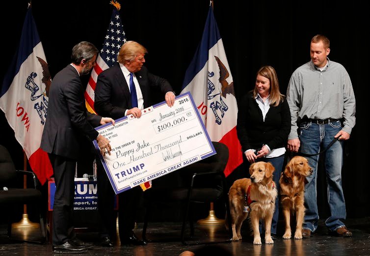 លោក Donald Trump កាន់មូលប្បទានប័ត្រធំមួយ ហើយប្រគល់ទៅស្ត្រីម្នាក់ដែលកាន់ខ្សែសម្រាប់ឆ្កែពីរក្បាល។