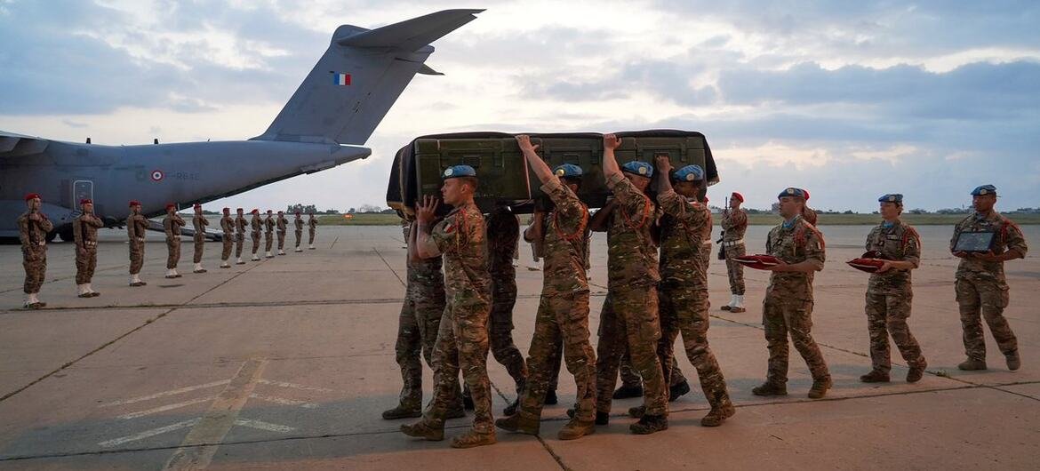 ទាហាន UNIFIL កាន់មឈូសនៅឯអាកាសយានដ្ឋានមួយ នៅផ្ទៃខាងក្រោយ ទាហានផ្សេងទៀតគោរពនៅក្បែរយន្តហោះដឹកជញ្ជូនយោធា។