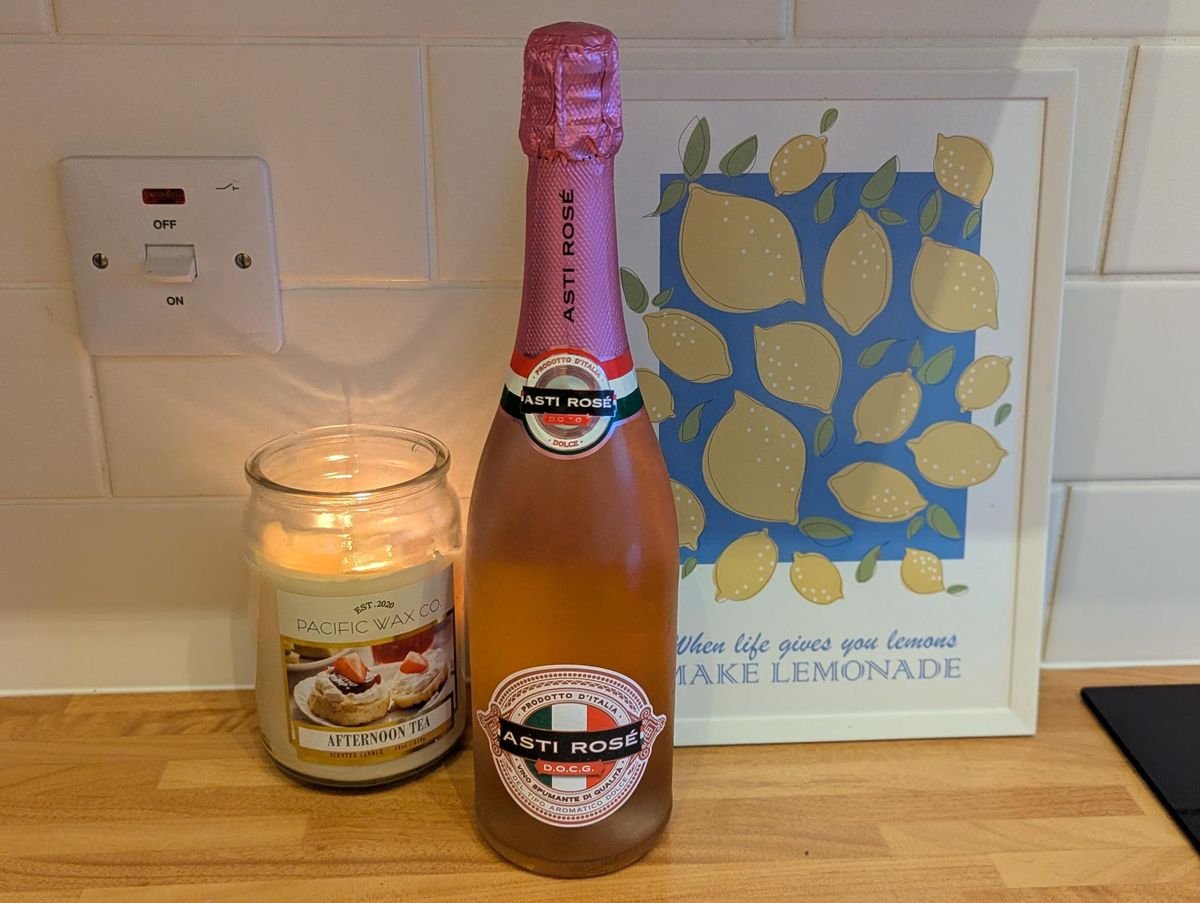 រូបភាពនៃដប Asti Rose Spumante DOCG នៅលើបញ្ជរផ្ទះបាយ ដែលមានទៀន និងរូបក្រូចឆ្មា
