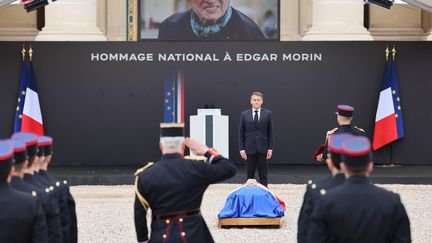 Emmanuel Macron នៅពីមុខមឈូសរបស់ Edgar Morin គ្របដណ្តប់ដោយទង់ជាតិបារាំងនៅឯ Invalides ក្នុងទីក្រុងប៉ារីសនៅថ្ងៃទី 6 ខែមិថុនាឆ្នាំ 2026 ក្នុងអំឡុងពេលពិធីកិត្តិយសជាតិ។ (LUDOVIC MARIN / AFP)