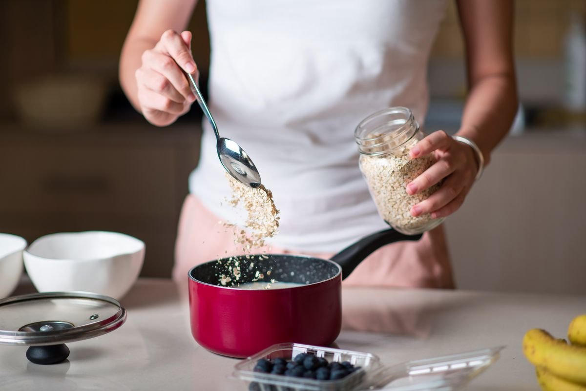 ស្ត្រីរៀបចំធញ្ញជាតិ oatmeal សម្រាប់អាហារពេលព្រឹកនៅក្នុងផ្ទះបាយនៅផ្ទះដោយបន្ថែមគ្រឿងផ្សំ។ រៀបចំអាហារសរីរាង្គដែលមានសុខភាពល្អ ពោរពេញដោយជាតិសរសៃ និងសារធាតុចិញ្ចឹម