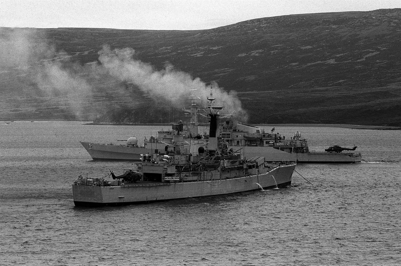 កប៉ាល់ Royal Navy បានចតនៅ Ajax Bay មួយថ្ងៃមុនពេលការផ្ទុះ និងលិចនៃ HMS Antelope (ផ្ទៃខាងក្រោយ) ។ Antelope ត្រូវ​បាន​បាញ់​ដោយ​កាំជ្រួច Exocet របស់​អាហ្សង់ទីន ដែល​ក្រោយ​មក​បាន​ផ្ទុះ​ខណៈ​ពេល​ដែល​ព្យាយាម​ការពារ​វា។